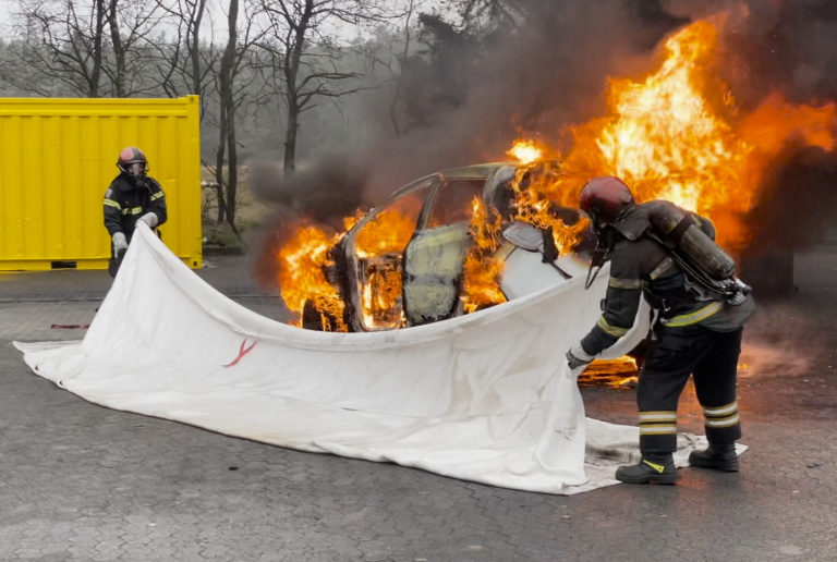 Fire Fighters covering a car on fire with a fire blanket